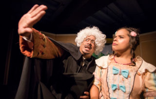 A Victorian Lord in a white wig and right hand outstretched in front of himself and the young maiden in a pink dress with many bows, mansplaining to her.