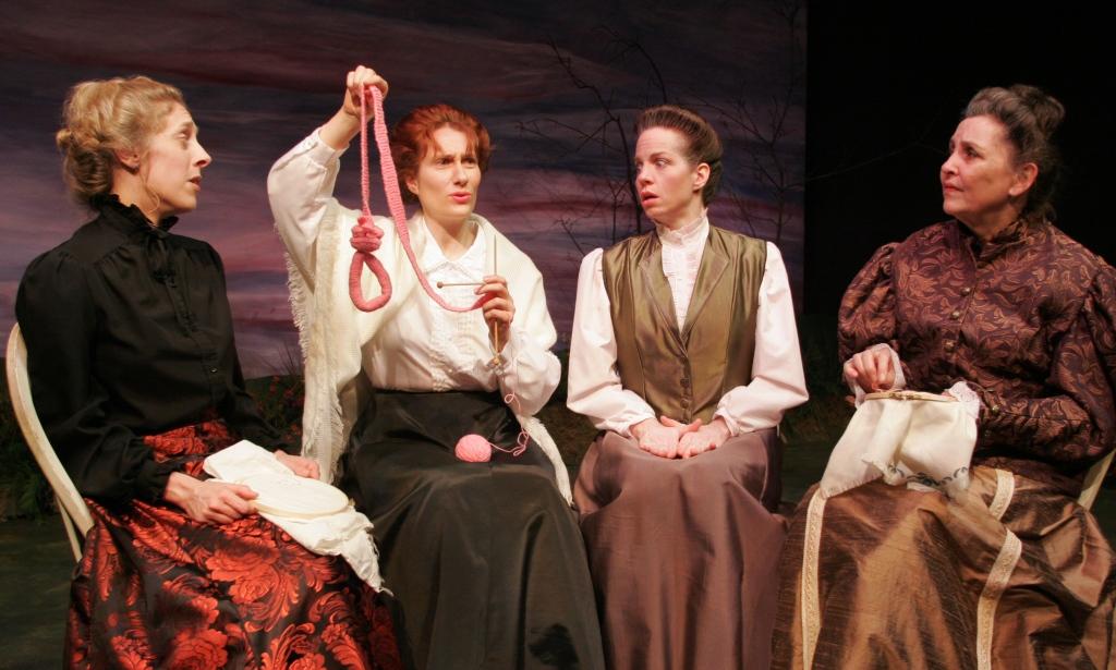 Four Victorian women sit side by side, one holds up a pink, hand-knit noose.