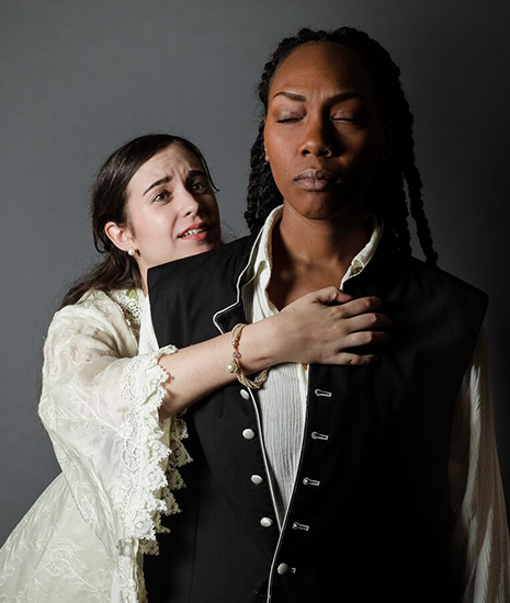 A white woman embracing, from behind, a black woman with her eyes closed