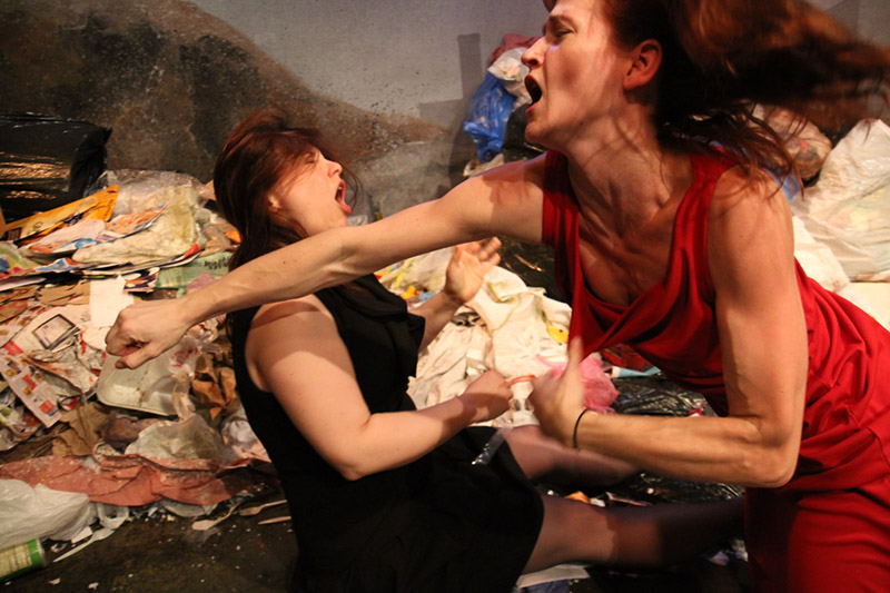 A woman in a red dress punching a woman in a black dress in the face