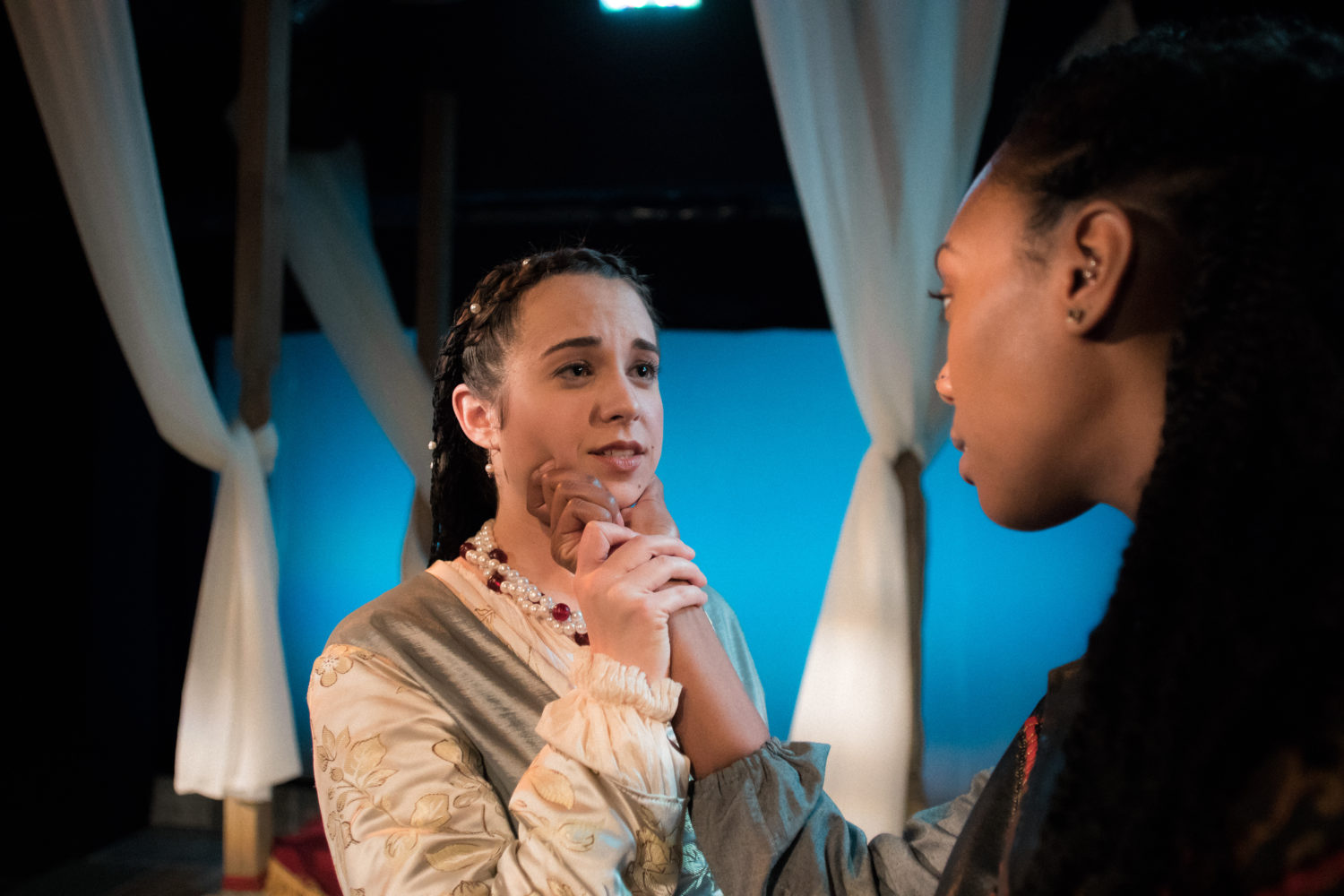 Othello holds Desdemona's face by the chin while Desdemona graps Othello's wrist