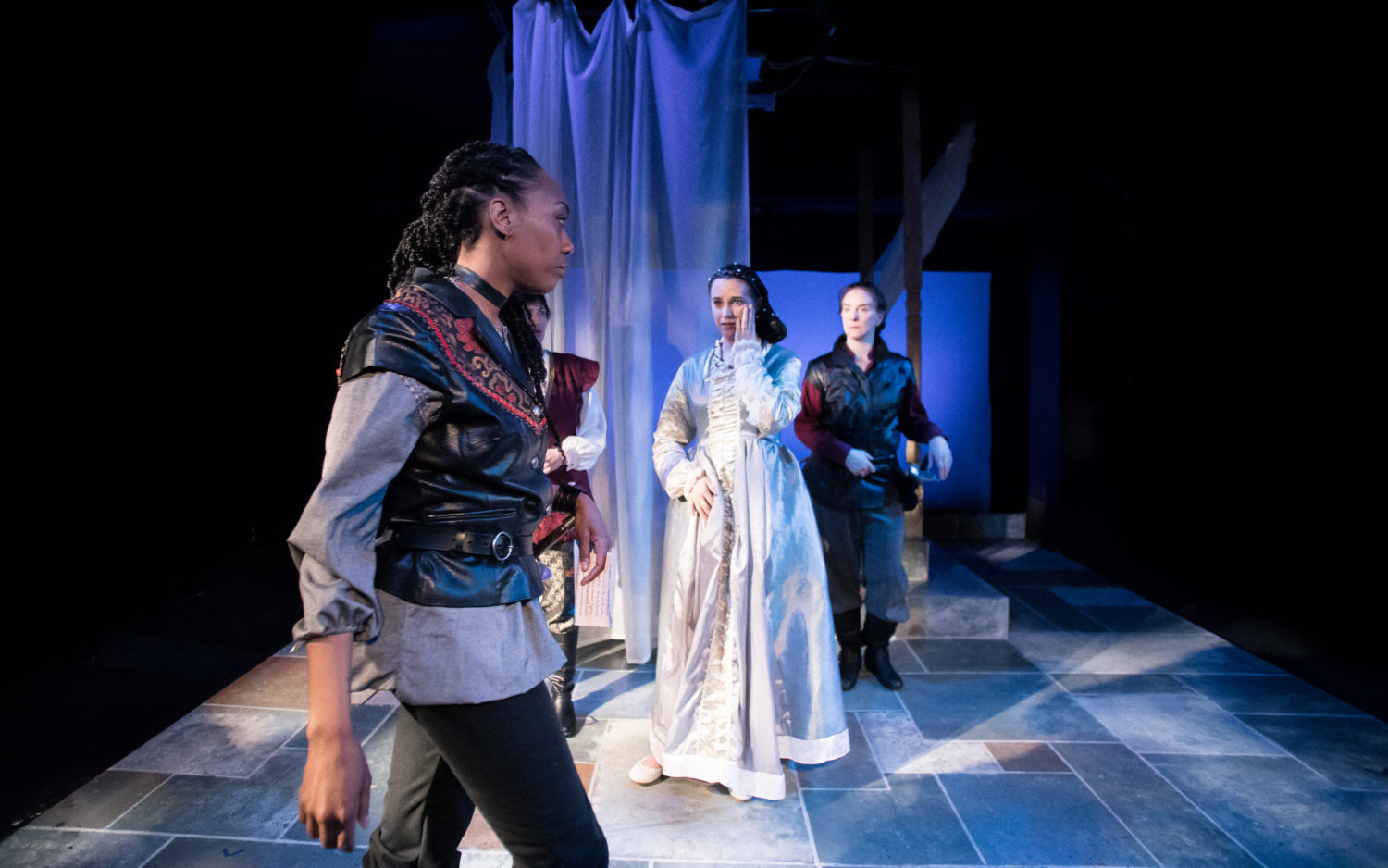 Othello walks away from Desdemona who is touching her face after being struck. Iago looks on.