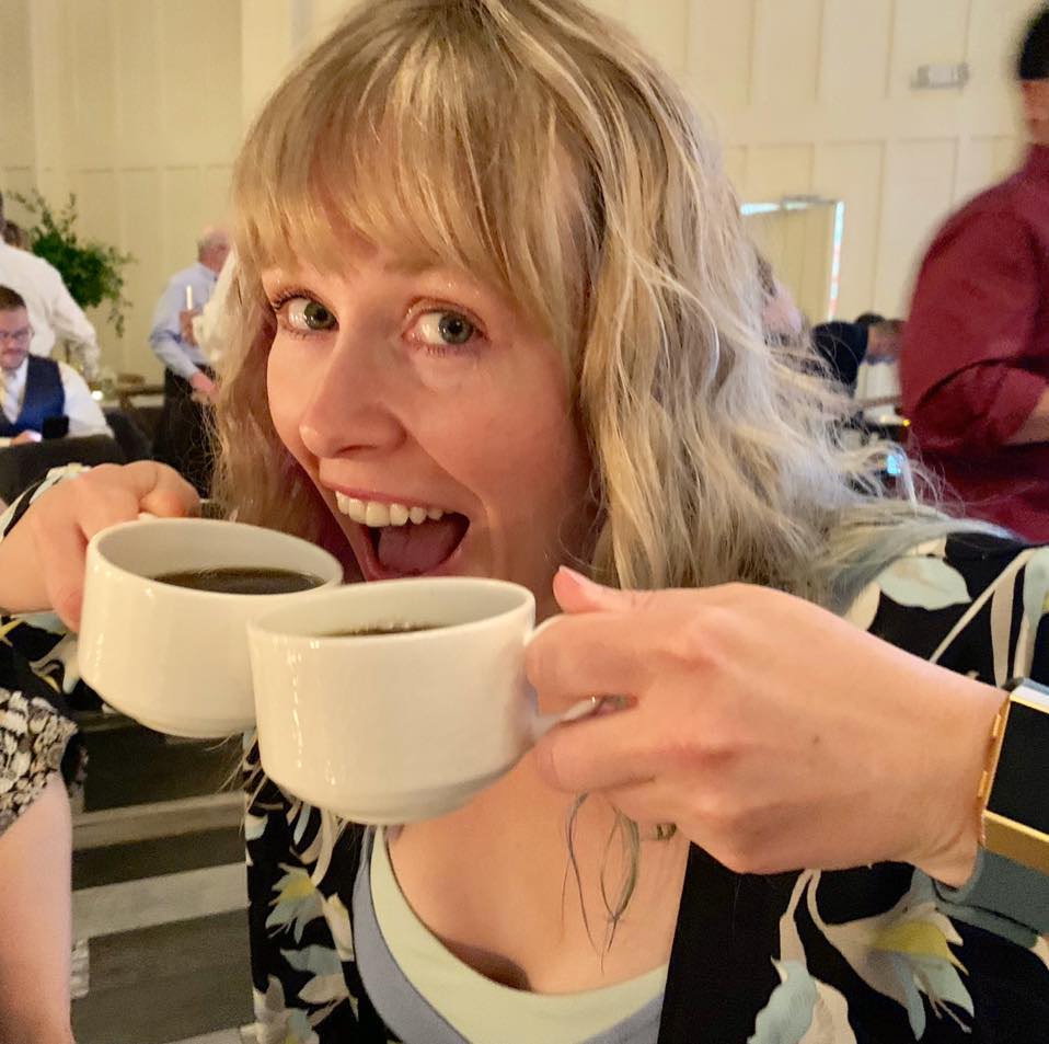 Woman holding and smiling over two cups of coffee by her face