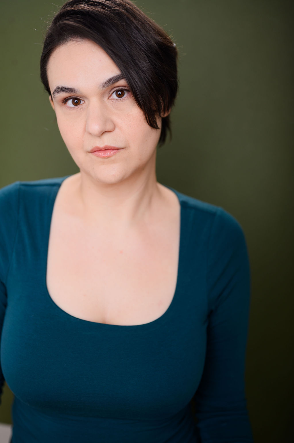 Woman with short, dark hair falling over the side of her face in a green shirt