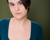 Woman with short, dark hair falling over the side of her face in a green shirt